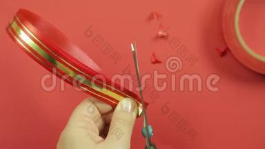 女人`手用一把剪刀剪一条红色丝带的角，用来做礼物蝴蝶结。 红色背景